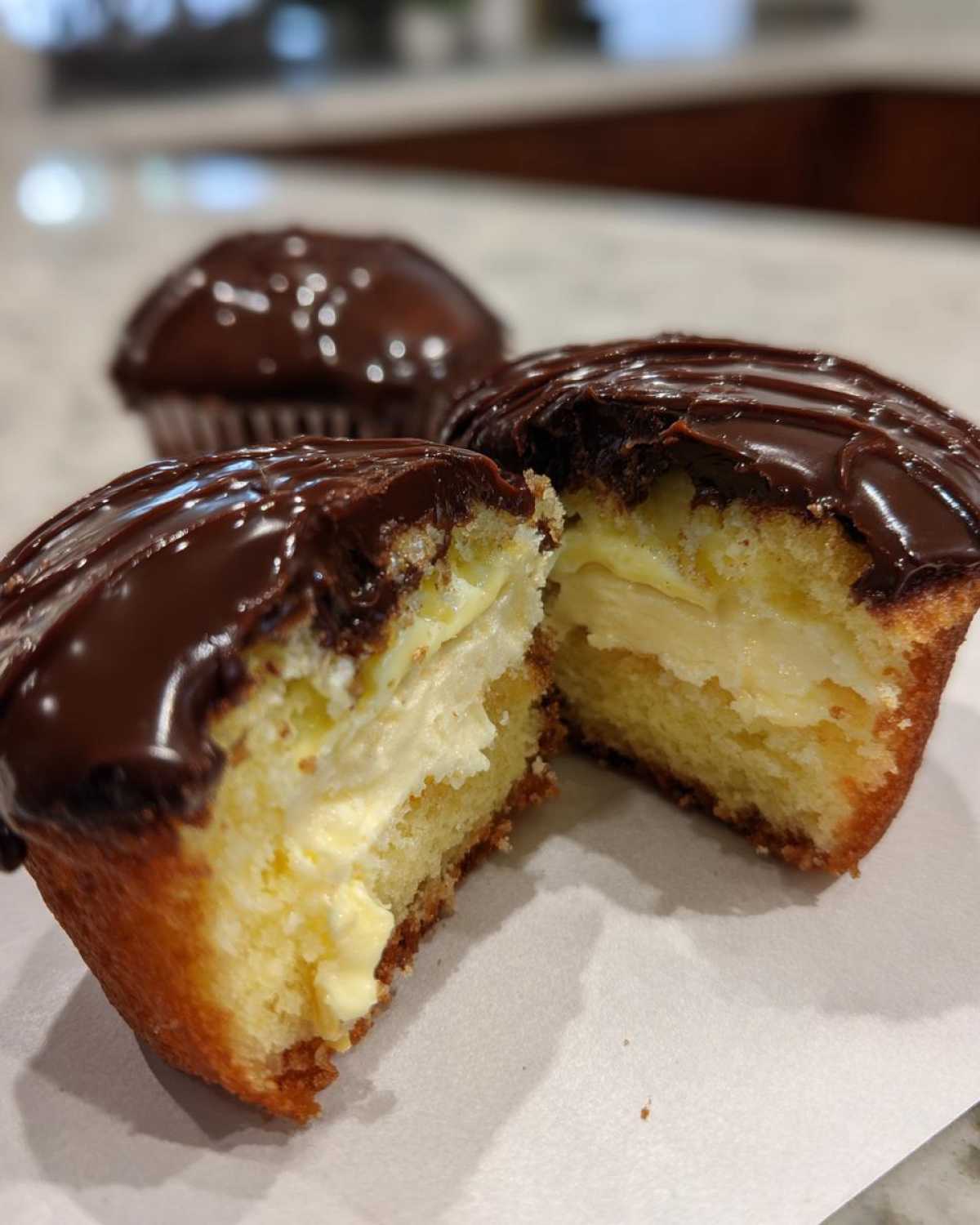 Close-up of boston cream pie cupcakes cut in half showing vanilla filling and chocolate glaze.