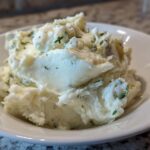 Close-up of creamy Boursin mashed potatoes mixed with herbs served in a white bowl.