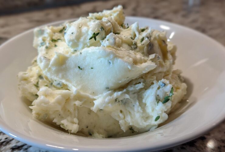 Close-up of creamy Boursin mashed potatoes mixed with herbs served in a white bowl.