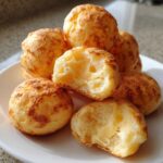 Close-up of golden brazilian cheese bread, one broken open showing a gooey, melted cheese center.
