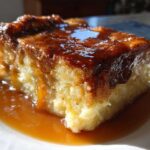 A close-up of a moist slice of bread pudding with bourbon sauce drizzled generously over the top.