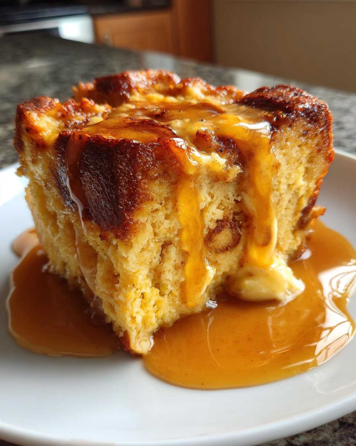 A close-up of a square slice of bread pudding with bourbon sauce drizzled over the top and pooling on the plate.