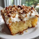 A close-up of a moist slice of butter pecan praline poke cake topped with thick white frosting and chopped pecans.