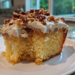 Close-up of a moist slice of butter pecan praline poke cake topped with frosting and candied pecans.