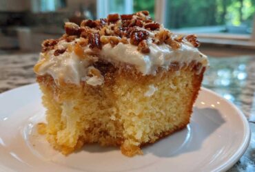 Close-up of a moist slice of butter pecan praline poke cake topped with frosting and candied pecans.