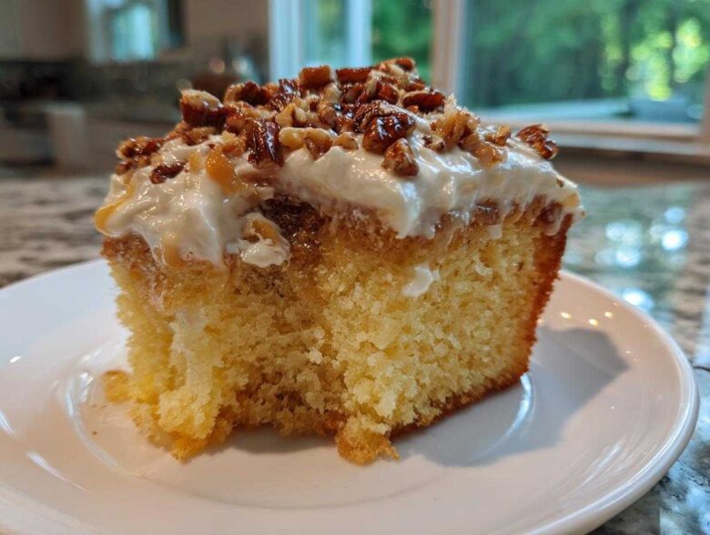 Close-up of a moist slice of butter pecan praline poke cake topped with frosting and candied pecans.