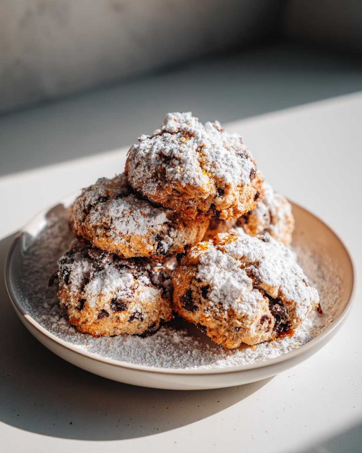 A stack of freshly baked cannoli cookies generously dusted with powdered sugar on a light plate.