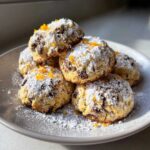 A stack of delicious cannoli cookies dusted heavily with powdered sugar and garnished with orange zest.