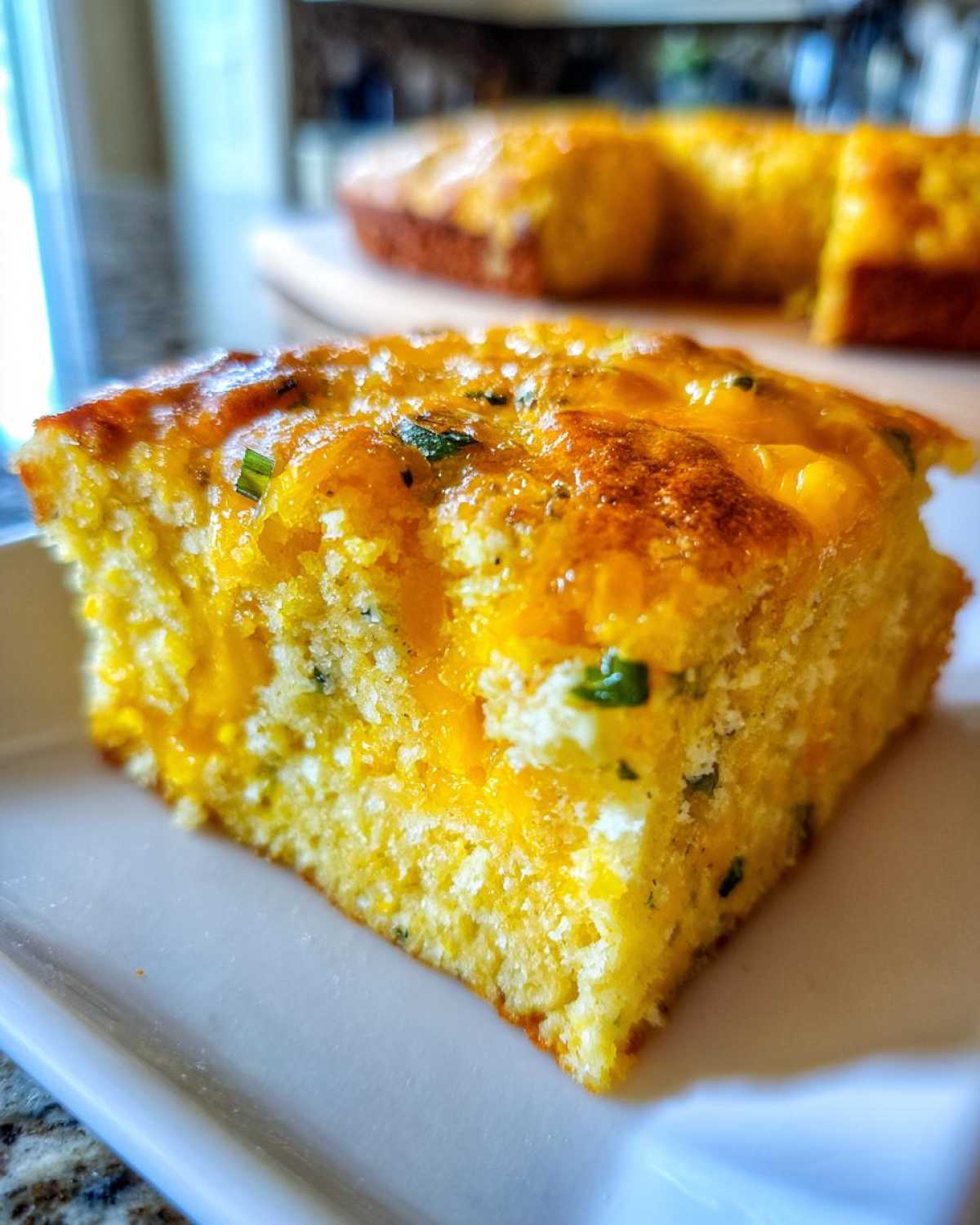 A close-up, appetizing slice of moist Mexican cornbread topped with melted cheddar cheese and green herbs.