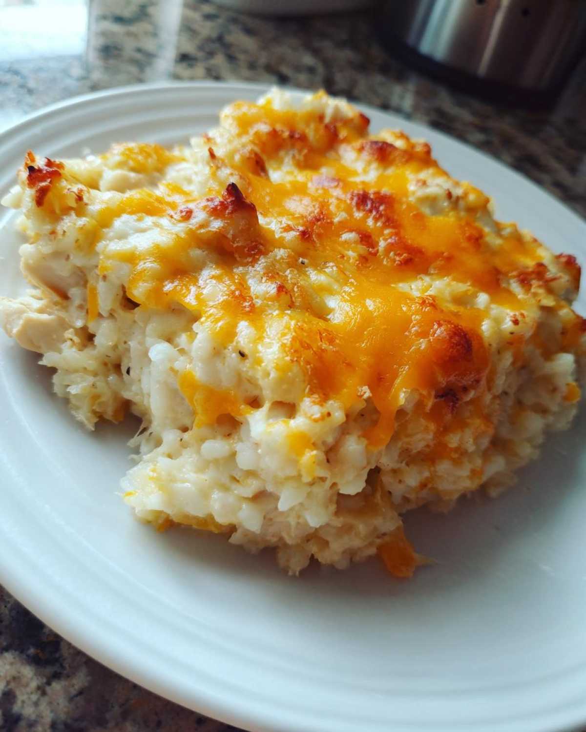 A close-up serving of creamy, cheesy rice casserole topped with melted, browned cheddar cheese.