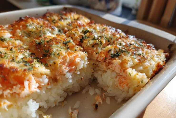 A close-up view of a freshly baked sushi bake with a golden, cheesy top and visible layers of rice and salmon.
