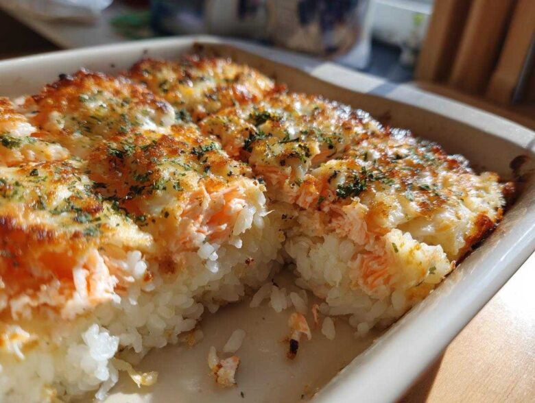 A close-up view of a freshly baked sushi bake with a golden, cheesy top and visible layers of rice and salmon.