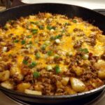 Close-up of Cheesy Taco Potatoes with ground meat, melted cheddar cheese, and green onions in a black cast iron skillet.