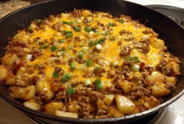 Close-up of Cheesy Taco Potatoes with ground meat, melted cheddar cheese, and green onions in a black cast iron skillet.