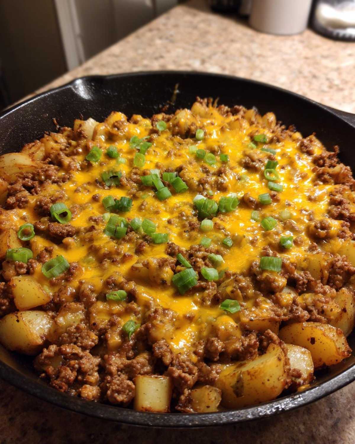 Close-up of Cheesy Taco Potatoes in a cast iron skillet, topped with melted cheddar and chopped green onions.