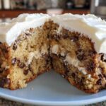 A thick, chewy cookie cake recipe slice cut in half, showing chocolate chips and creamy white frosting.