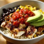 Close-up of a hearty chicken burrito bowl featuring seasoned chicken, rice, black beans, corn, salsa, and sliced avocado.