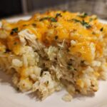 Close-up of a serving of chicken cauliflower rice casserole topped with melted cheddar cheese and parsley.