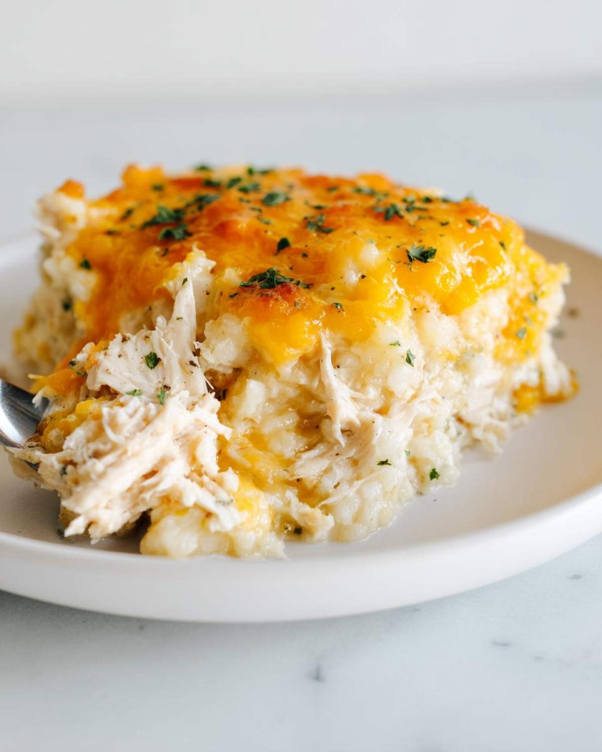 A serving of creamy chicken cauliflower rice casserole topped with melted cheddar cheese and parsley, being lifted by a fork.