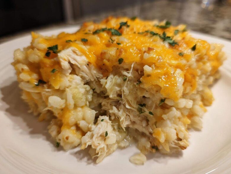 Close-up of a serving of chicken cauliflower rice casserole topped with melted cheddar cheese and parsley.