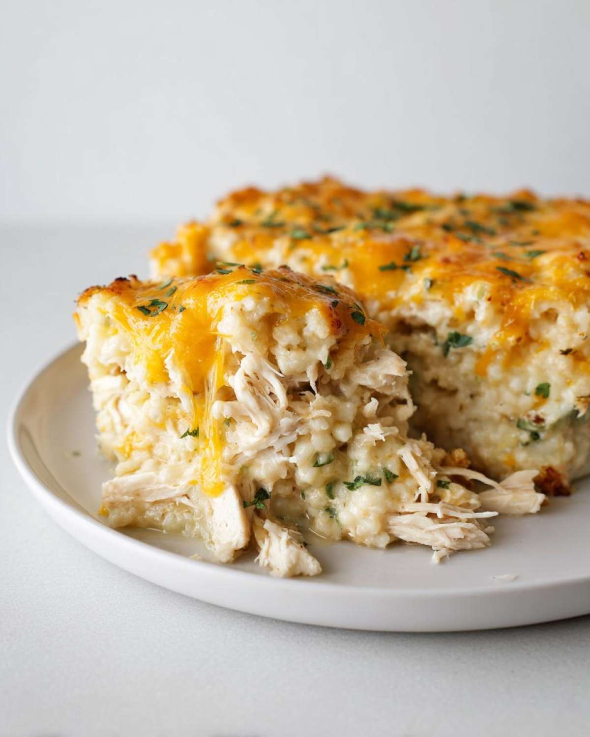 A slice of creamy chicken cauliflower rice casserole topped with melted cheddar cheese and parsley.