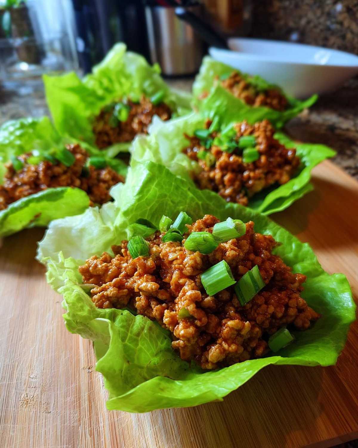 Close-up of several chicken lettuce wraps filled with savory ground chicken mixture and topped with green onions.
