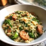 Close-up of creamy chicken sausage and broccoli orzo served in a white bowl, garnished with fresh herbs.