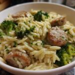 Close-up of a white bowl filled with creamy chicken sausage and broccoli orzo, garnished with parsley.