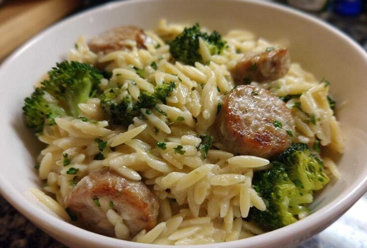 Close-up of a white bowl filled with creamy chicken sausage and broccoli orzo, garnished with parsley.