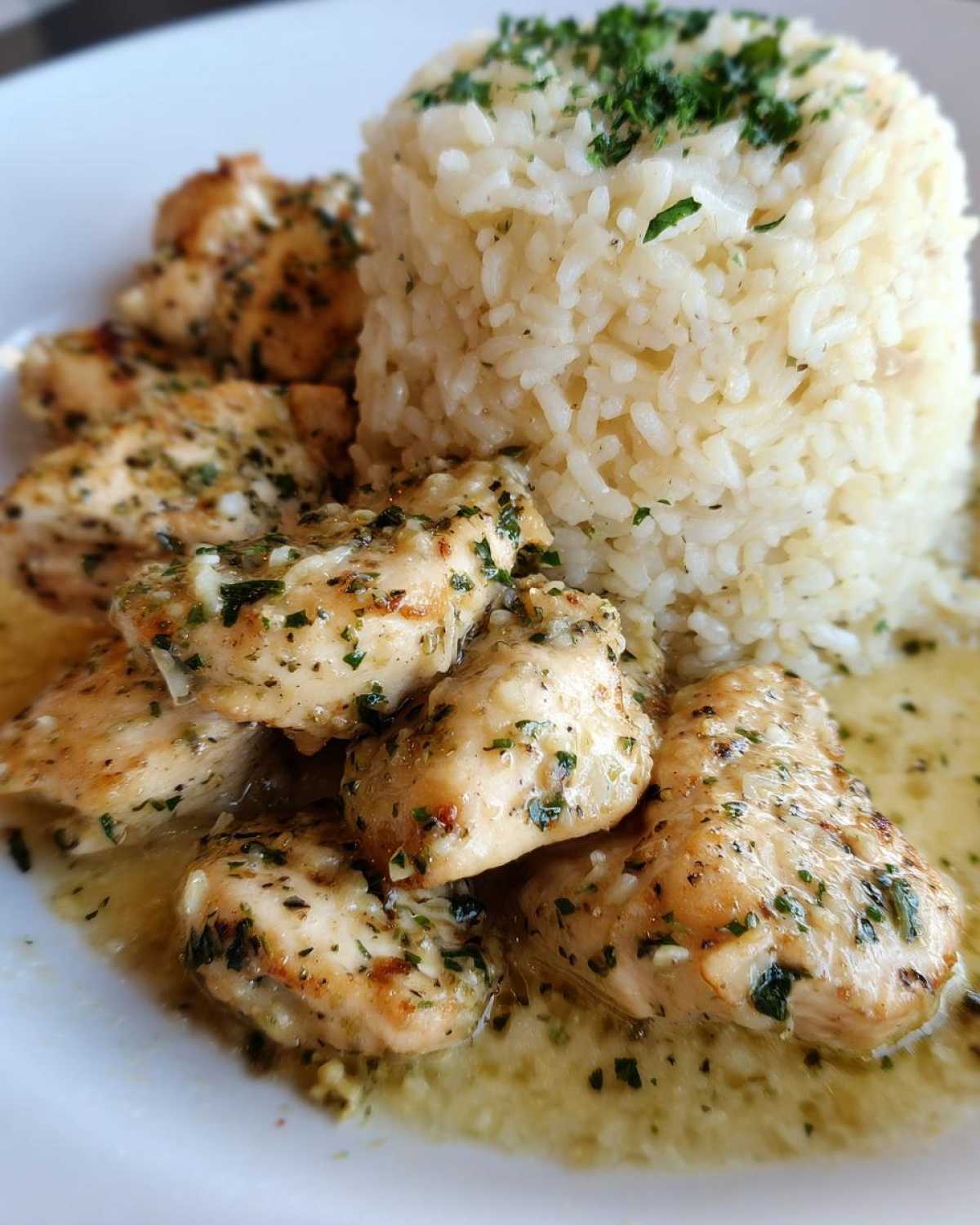 Close-up of juicy chicken scampi pieces served next to a molded portion of garlic parmesan rice.