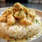 Close-up of tender chicken scampi pieces served over a mound of garlic parmesan rice, drizzled with sauce.