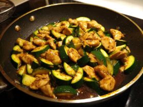 Close-up of chicken zucchini stir fry cooking in a dark skillet with a glossy brown sauce.
