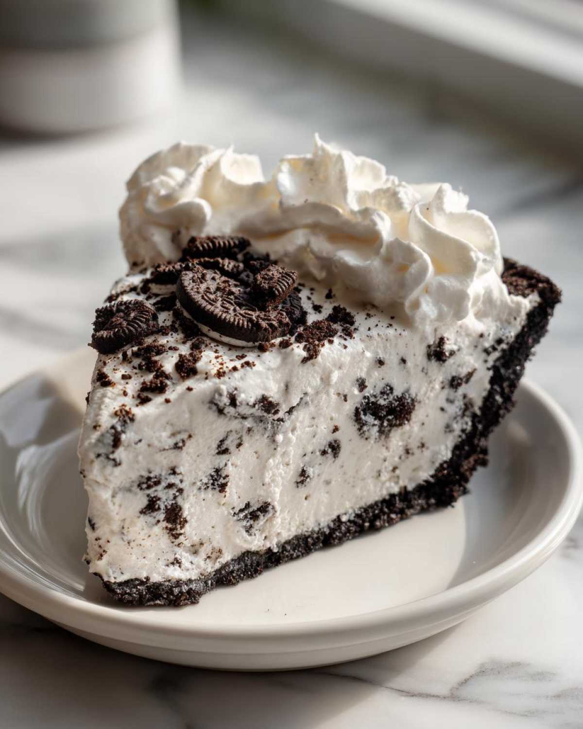 A generous slice of cookies and cream ice cream pie topped with whipped cream and mini cookies.