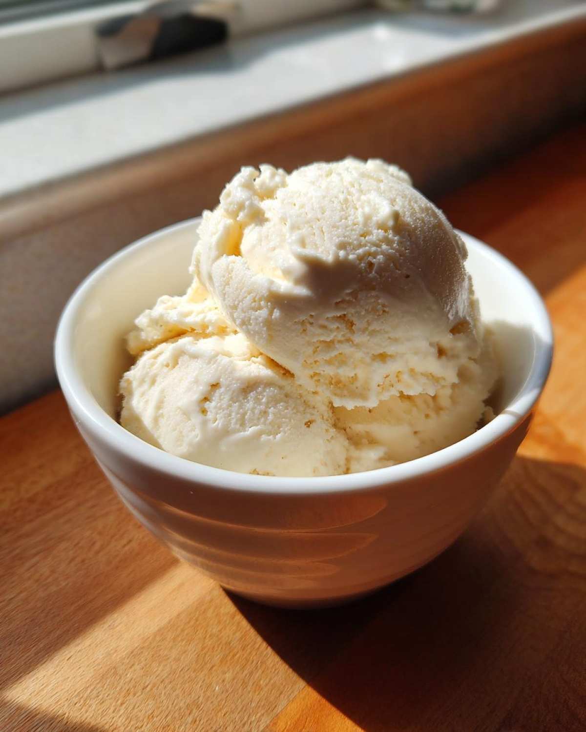 Two scoops of creamy, pale yellow cottage cheese ice cream served in a small white bowl.