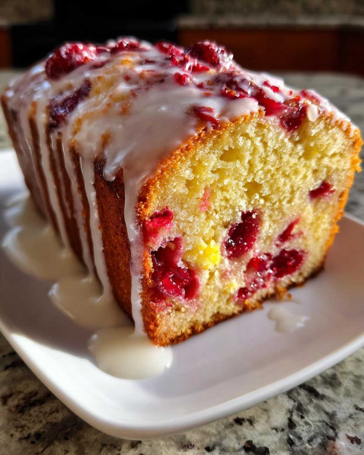 Close-up of a slice of moist cranberry orange bread topped with a thick vanilla glaze and whole cranberries.