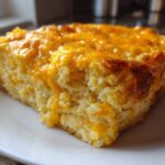 A thick, golden slice of baked cheese grits casserole topped with melted cheddar cheese.