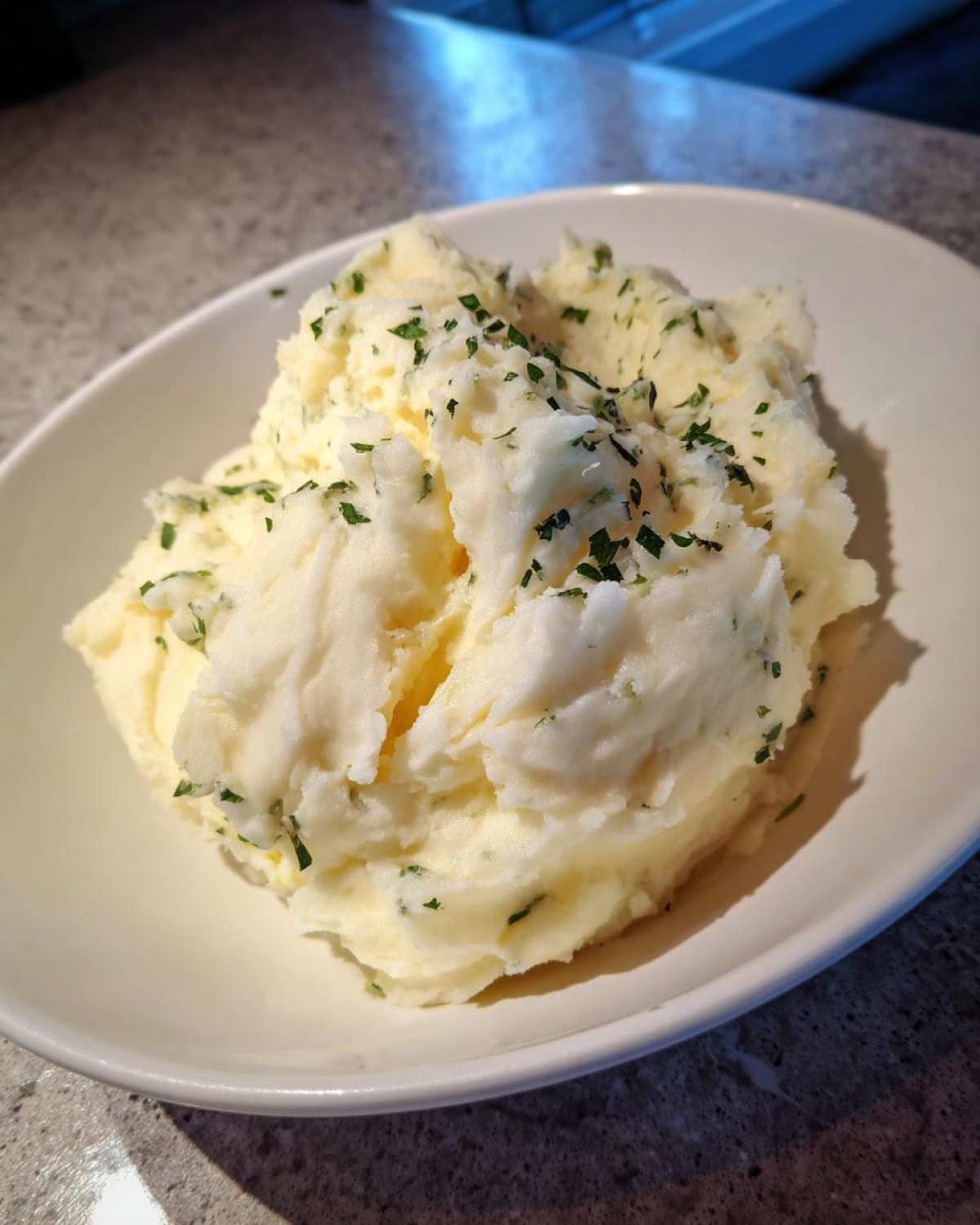 A close-up of creamy Boursin mashed potatoes served in a white bowl and topped with chopped fresh parsley.
