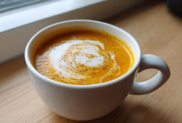 A close-up of creamy, orange butternut squash soup topped with a swirl of cream and cracked black pepper.