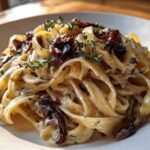 Close-up of creamy fettuccine pasta tossed with rich caramelized onion pasta, garnished with fresh thyme sprigs.