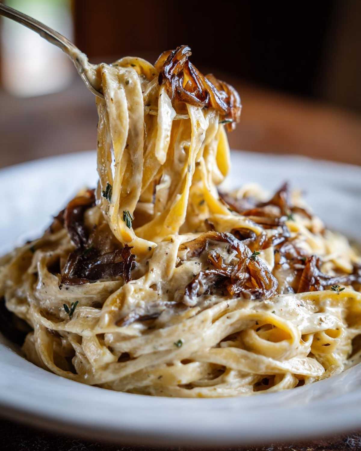 A fork lifting a twirl of creamy fettuccine pasta topped with rich caramelized onion pasta.