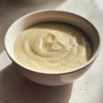 Close-up of a white bowl filled with creamy, smooth cauliflower soup, lightly seasoned.