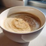 A close-up of creamy cauliflower soup in a white bowl, swirled and dusted with nutmeg or pepper.