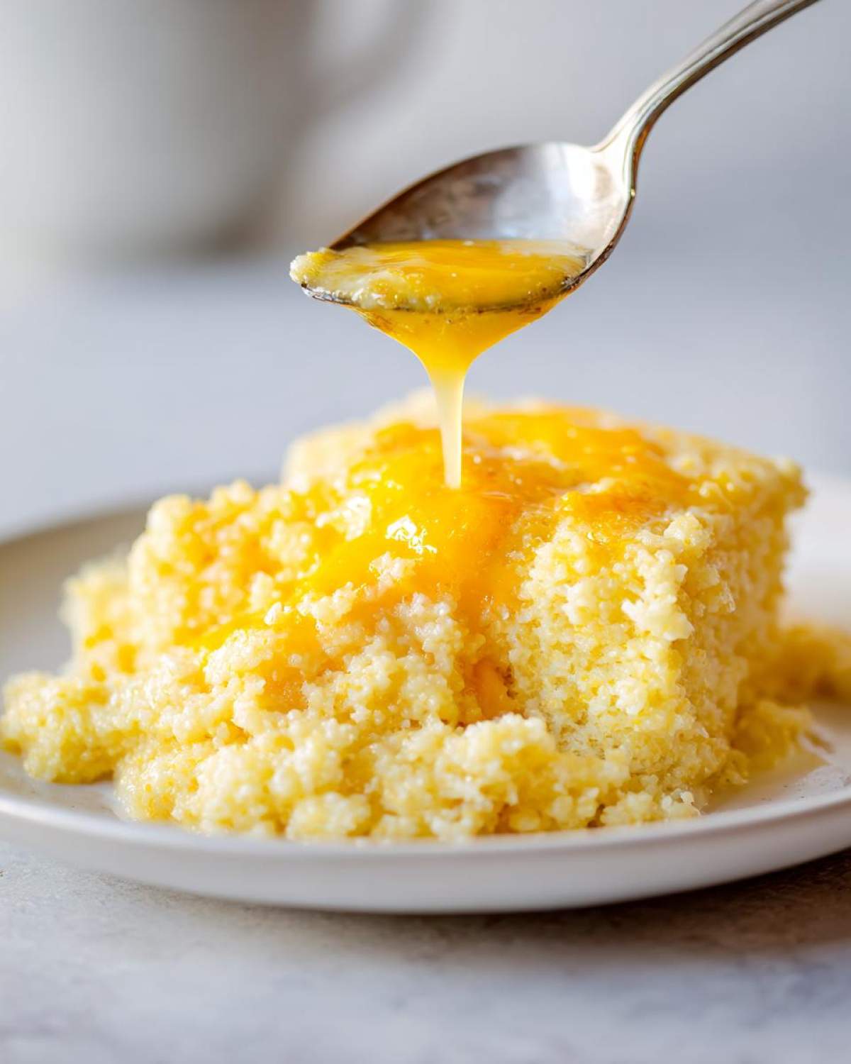 A spoonful of melted butter is drizzled over a serving of creamy cheese grits on a white plate.