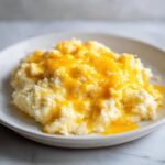 A close-up of creamy cheese grits topped with a generous layer of melted, bright orange cheddar cheese.