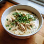 A close-up of creamy chicken chili, featuring shredded chicken and topped generously with fresh green parsley.
