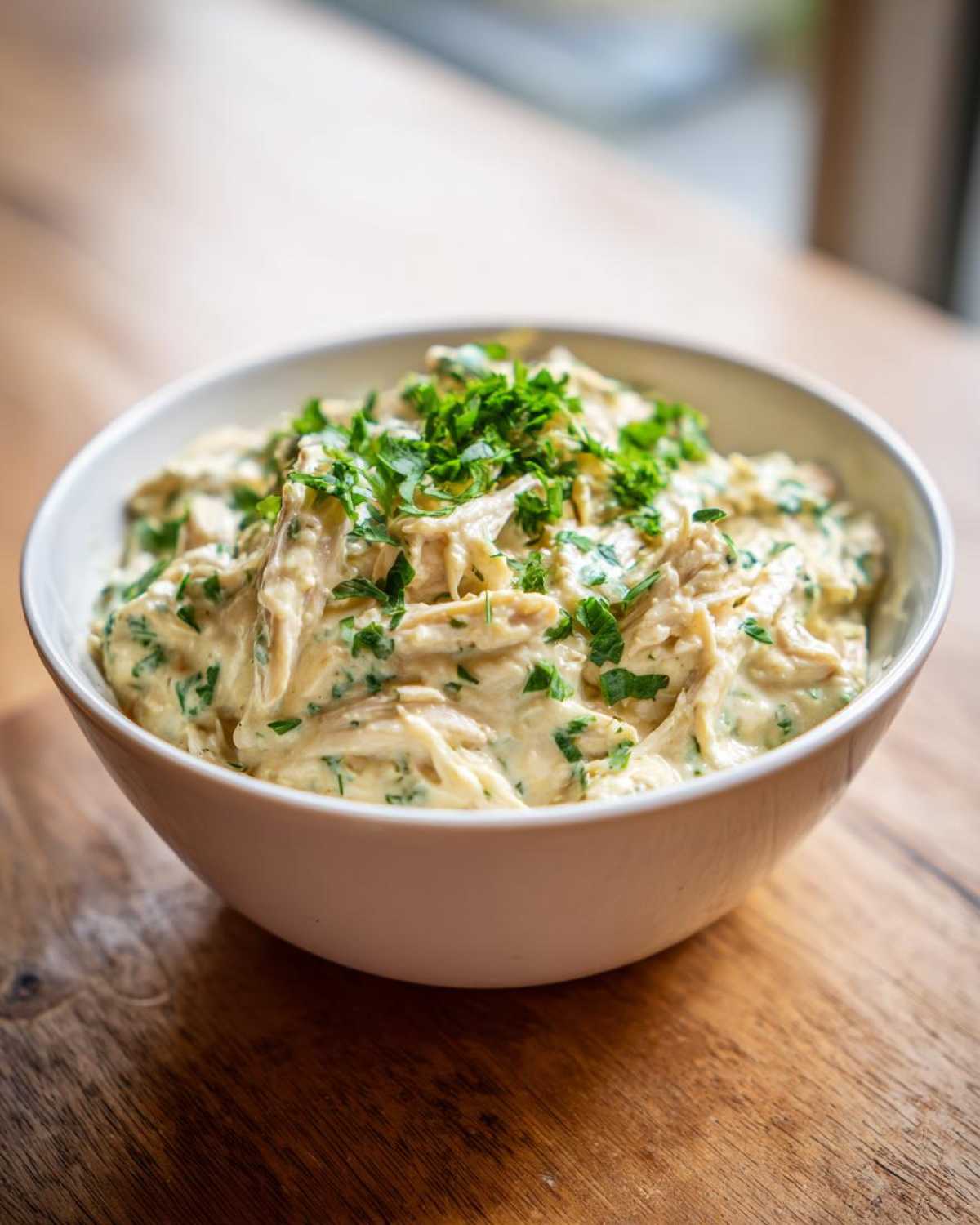 A close-up of creamy chicken chili filling, topped generously with fresh chopped parsley, served in a white bowl.