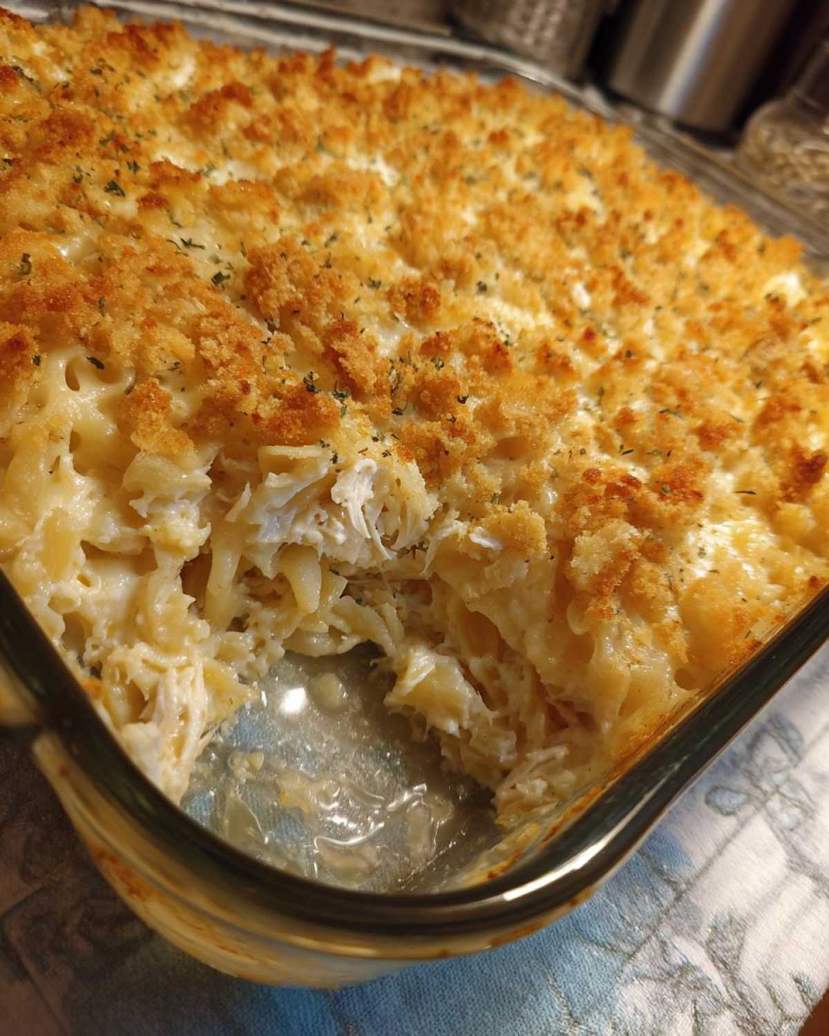 Close-up of a creamy chicken noodle casserole with a golden, crunchy breadcrumb topping, showing a portion taken out.