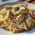 A close-up of creamy chicken pasta featuring fettuccine noodles, diced seasoned chicken, and grated Parmesan cheese.
