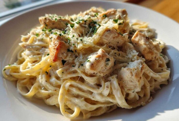 A close-up of creamy chicken pasta featuring fettuccine noodles, diced seasoned chicken, and grated Parmesan cheese.