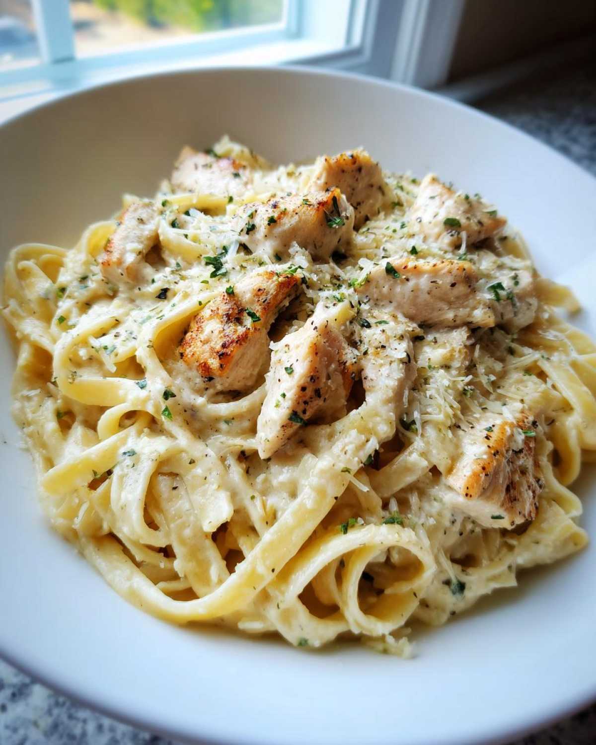 Close-up of creamy chicken pasta featuring fettuccine, seasoned chicken pieces, and grated parmesan cheese.
